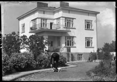Ukończony dom Fryderyka Janusza na archiwalnej fotografii rodzinnej. Zdjęcie wykonane od strony południowej ukazuje eksponowane na słońce elewacje południowo-wschodnią i południowo-zachodnią, powiązane obszernym narożnym podcieniem na parterze i usytuowanym nad nim tarasem. Świadome projektowanie pokoi dziennych po najbardziej nasłonecznionej stronie oraz wiązanie mieszkania z naturalnym otoczeniem było w&oacute;wczas                  w lokalnej praktyce budowlanej bardzo nowatorskie. Zdjęcie ze zbior&oacute;w Galerii Fotografii Miasta Rzeszowa
